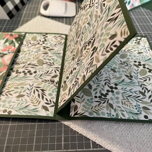 Puede incluir: Una tarjeta con un patr&oacute;n verde y blanco con un dise&ntilde;o floral. La tarjeta est&aacute; doblada por la mitad y tiene un borde verde.