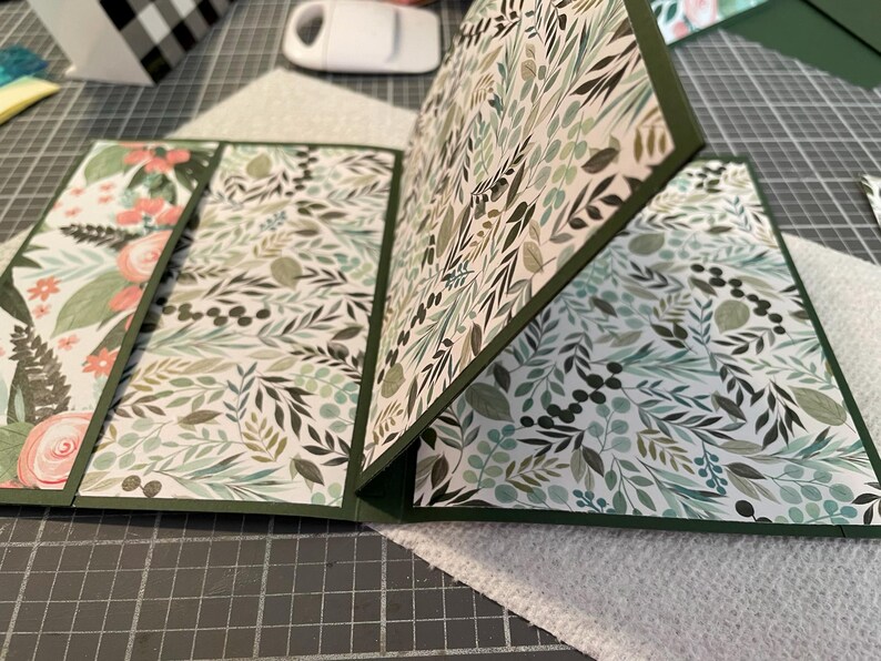 Puede incluir: Una tarjeta con un patr&oacute;n verde y blanco con un dise&ntilde;o floral. La tarjeta est&aacute; doblada por la mitad y tiene un borde verde.