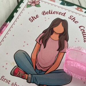 Puede incluir: Una tarjeta rosa y blanca con una ilustraci&oacute;n de dibujos animados de una ni&ntilde;a sentada con las piernas cruzadas. El texto en la tarjeta dice "Ella cre&iacute;a que pod&iacute;a, pero primero ten&iacute;a que creer en s&iacute; misma."
