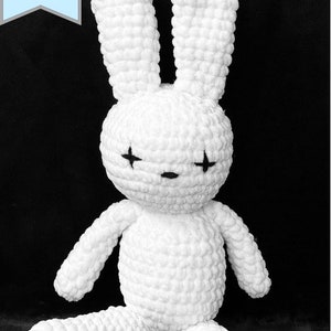 May include: White crocheted bunny rabbit with black embroidered eyes. The bunny is sitting with its legs crossed.
