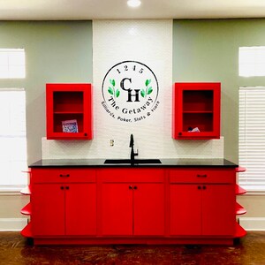 May include: Red cabinets with black handles and a black countertop with a sink. The wall behind the cabinets has a white tile backsplash and a black and white logo that says "The Getaway Billiards, Poker, Slots & More".