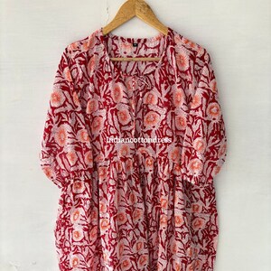 May include: A red cotton dress with a white floral print. The dress has a round neckline and 3/4 sleeves. The dress is hanging on a wooden hanger.
