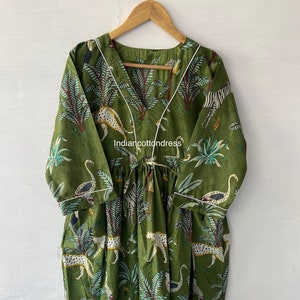 May include: A green cotton dress with a white trim and a jungle print featuring leopards, zebras, birds, and palm trees. The dress has a V-neckline and a tie at the waist. The text "Indiancottondress" is visible on the dress.