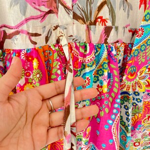 May include: A pink and white dress with a floral print and a tie at the waist. The dress has a paisley pattern on the bottom half.