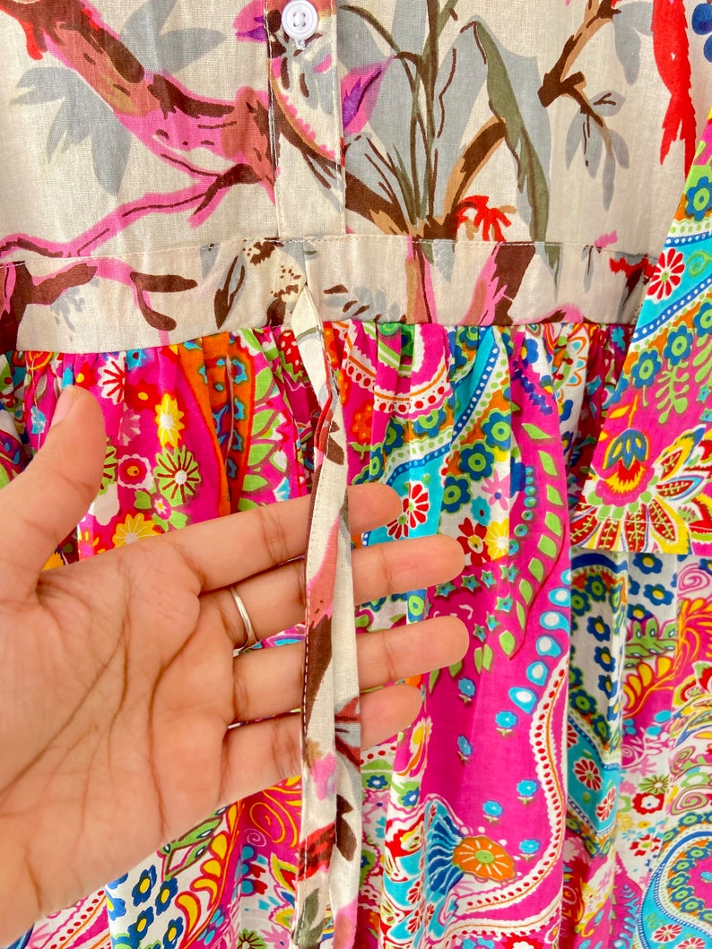 May include: A pink and white dress with a floral print and a tie at the waist. The dress has a paisley pattern on the bottom half.
