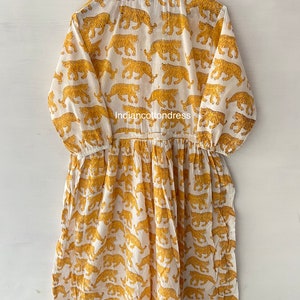 May include: A white cotton dress with a yellow tiger print. The dress has a round neckline and 3/4 sleeves. The dress is gathered at the waist and has a flowing skirt.