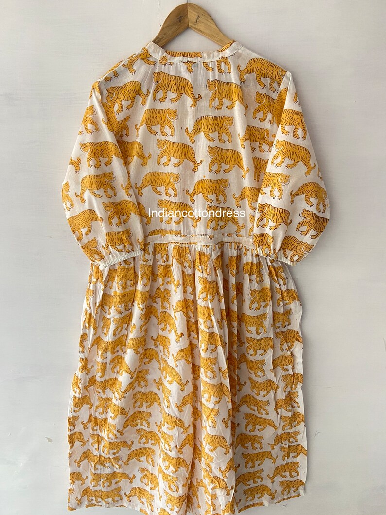 May include: A white cotton dress with a yellow tiger print. The dress has a round neckline and 3/4 sleeves. The dress is gathered at the waist and has a flowing skirt.