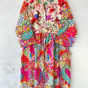 May include: A long-sleeved, colorful dress with a paisley print. The dress has a button-up front and a gathered waist. The fabric is a blend of cotton and silk.
