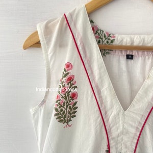 May include: White sleeveless top with a pink floral print and red trim around the neckline. The top has a V-neck and is labeled size "M".