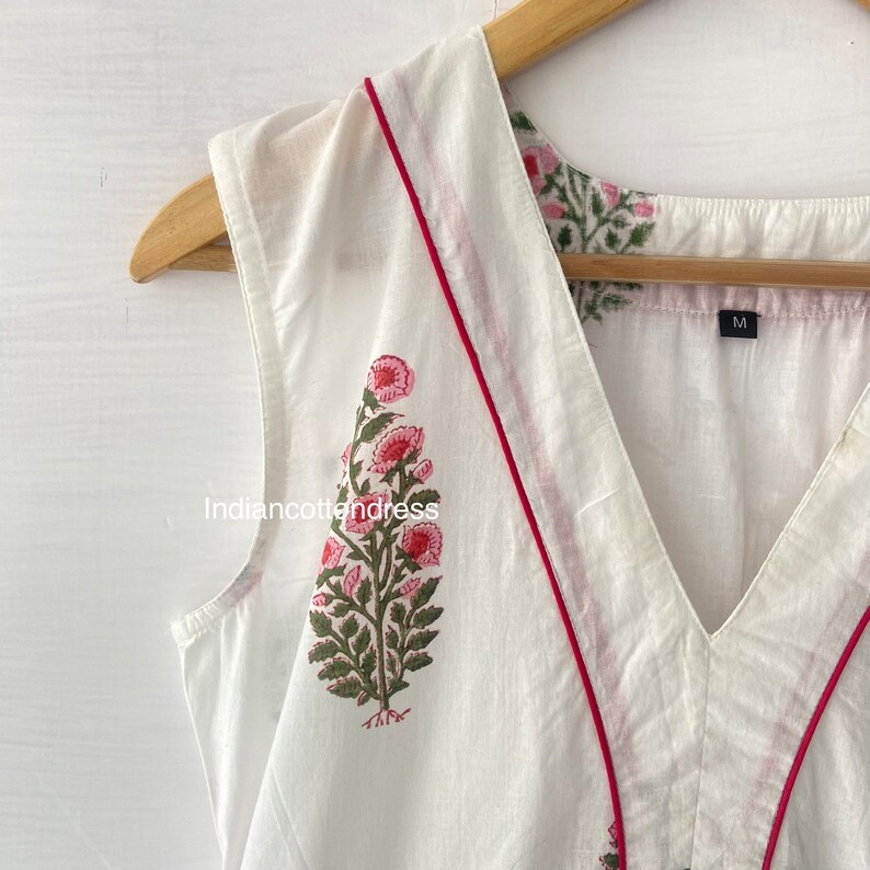 May include: White sleeveless top with a pink floral print and red trim around the neckline. The top has a V-neck and is labeled size "M".
