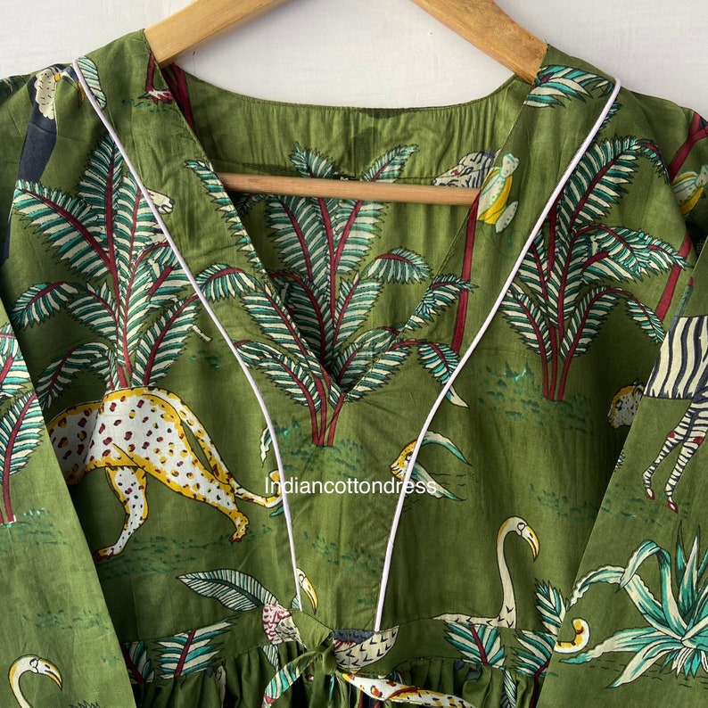 May include: Green cotton dress with a V-neck and white piping. The dress features a jungle print with leopards, zebras, flamingos, and palm trees.