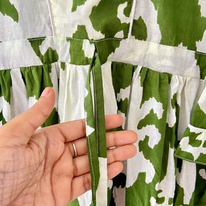 May include: A white and green dress with a tie at the back. The dress has a floral pattern.