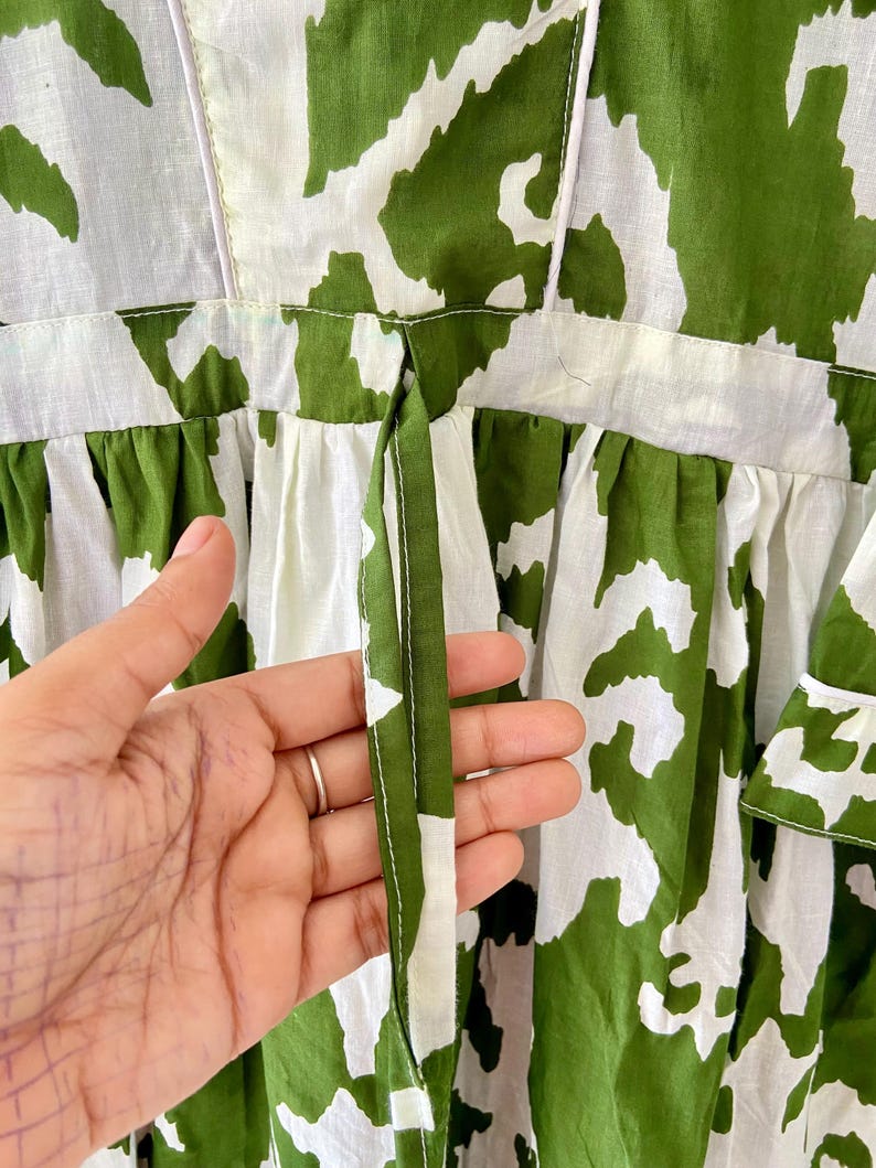 May include: A white and green dress with a tie at the back. The dress has a floral pattern.