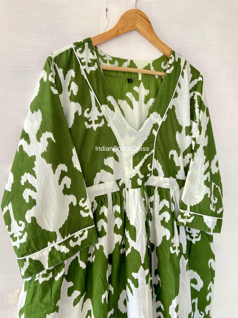 May include: A green and white printed cotton dress with a V-neckline and 3/4 sleeves. The dress has a gathered waist and a relaxed fit. The fabric is soft and comfortable. "IndianCottonDress" is printed on the dress.