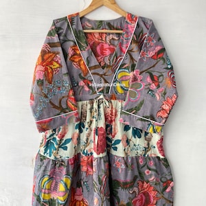 May include: A gray cotton dress with a floral print. The dress has a V-neckline and 3/4 sleeves. The dress is tiered and has a tie at the waist. The dress is made of 100% cotton and is machine washable.