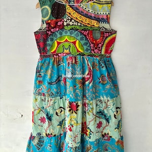 May include: A sleeveless maxi dress with a patchwork design featuring various colors and patterns, including red, green, blue, yellow, and white. The dress has a tiered skirt and a white trim around the neckline. The text "Indian Cotton Dress" is visible on the dress.