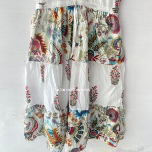 May include: White cotton dress with a tiered skirt featuring a colorful floral print. The dress has a drawstring waist and a relaxed fit.