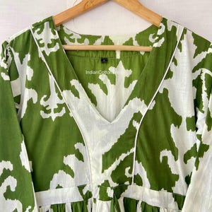 May include: Green and white printed cotton dress with a V-neckline and 3/4 sleeves. The dress has a tie at the waist and a ruffled hem. The label on the dress reads "IndianCottonWear".