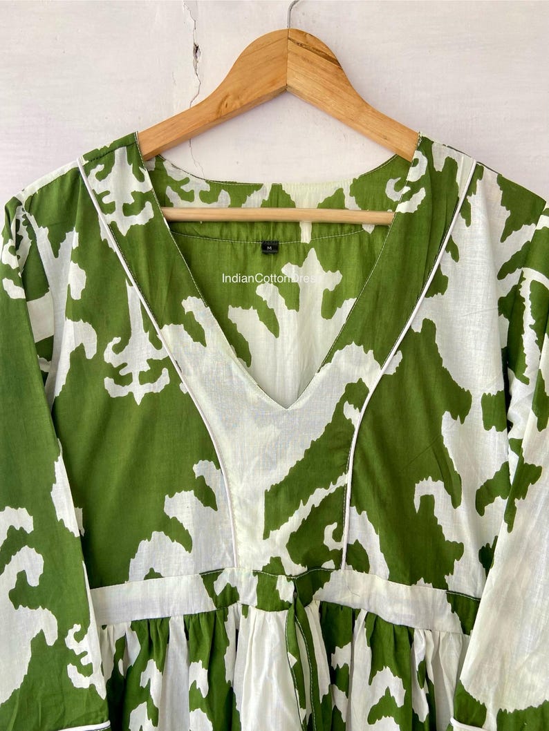May include: Green and white printed cotton dress with a V-neckline and 3/4 sleeves. The dress has a tie at the waist and a ruffled hem. The label on the dress reads "IndianCottonWear".