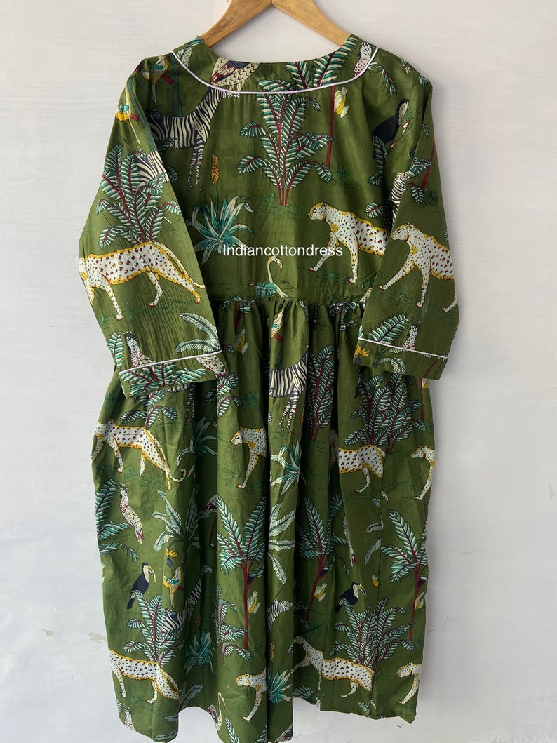May include: A green cotton dress with a white trim. The dress features a print of leopards, zebras, and tropical plants. The text "indiancottondress" is printed on the dress.