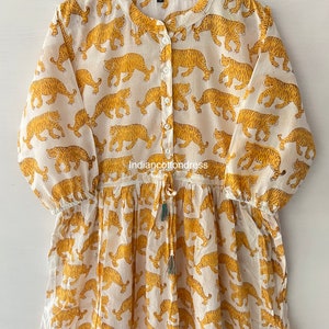 May include: A white cotton dress with a yellow tiger print. The dress has a button-up front, long sleeves, and a drawstring waist.