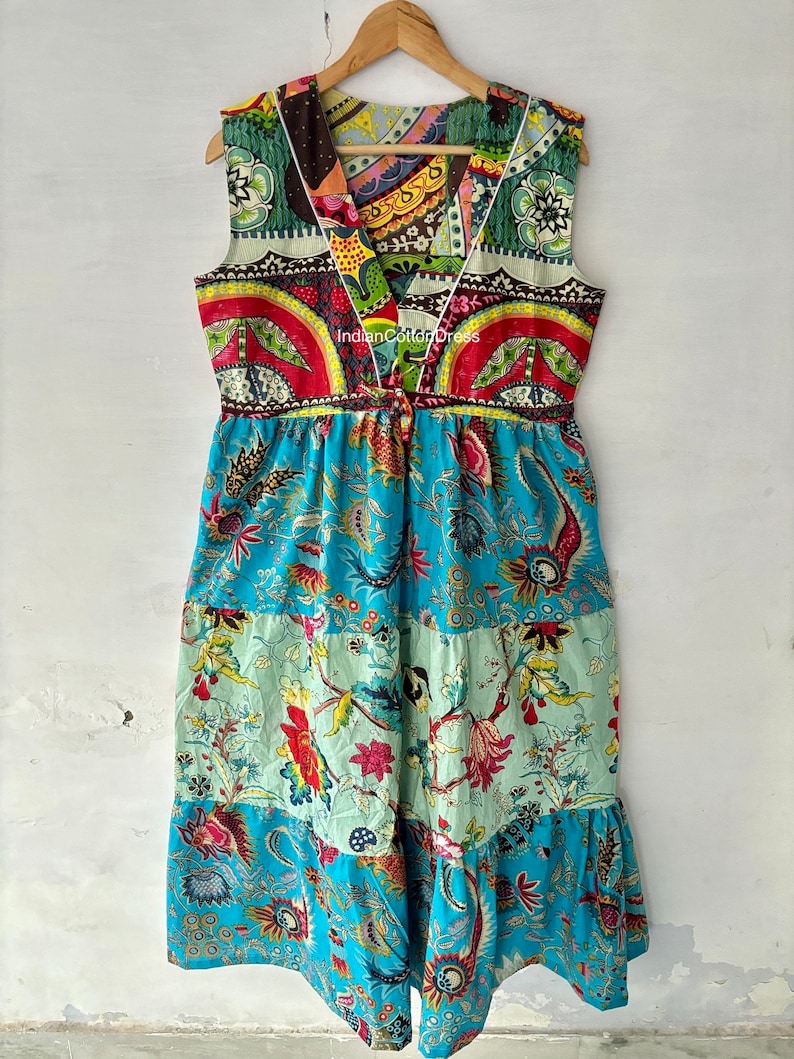 May include: A long, sleeveless, patchwork dress with a V-neckline. The dress is made of colorful cotton fabric with floral and geometric patterns. The dress has a tiered skirt and a tie at the waist. The text "Indian Cotton Dress" is visible on the dress.