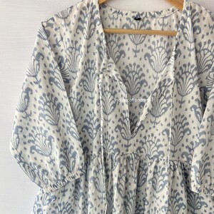 May include: A white and blue cotton tunic with a tie-front neckline and a floral print. The tunic has a gathered skirt and 3/4 sleeves.