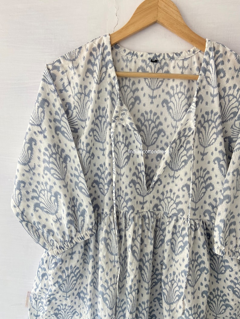 May include: A white and blue cotton tunic with a tie-front neckline and a floral print. The tunic has a gathered skirt and 3/4 sleeves.