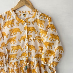 May include: A white cotton dress with a yellow tiger print. The dress has a button-up front, long sleeves, and a drawstring waist.