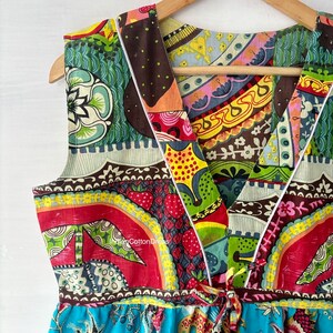 May include: A colorful, patterned sleeveless dress with a V-neckline and a tie at the waist. The dress is made of cotton and has a patchwork design.