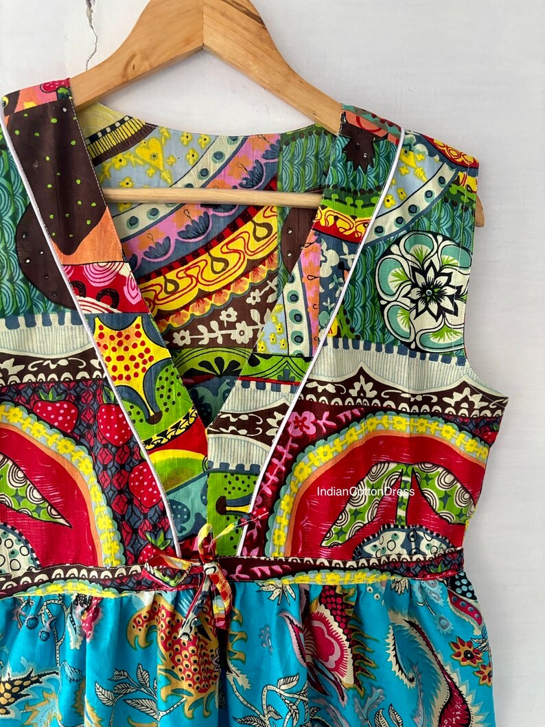May include: A colorful, patterned, sleeveless dress with a V-neckline and a tie at the waist. The dress is made of cotton and has a blue floral print on the bottom.