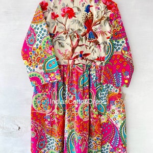 May include: A long-sleeved pink dress with a paisley print. The dress has a white floral print on the top half with a bird design. The dress is made of cotton.