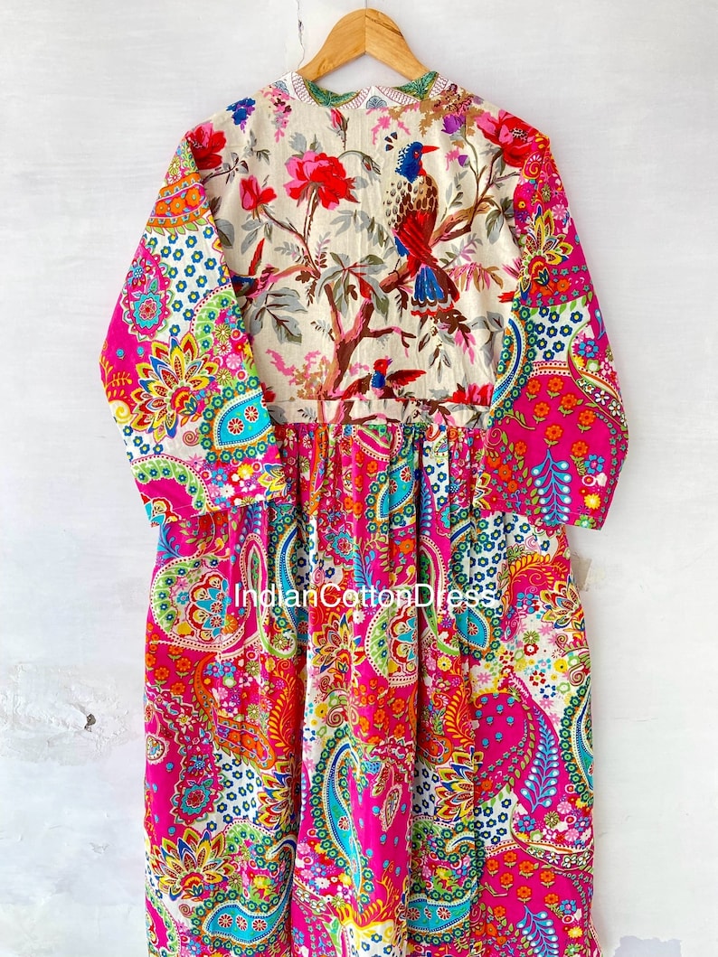 May include: A long-sleeved pink dress with a paisley print. The dress has a white floral print on the top half with a bird design. The dress is made of cotton.