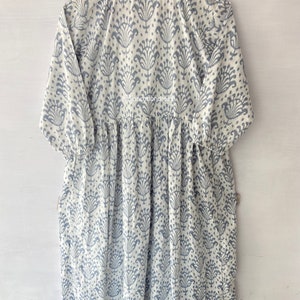 May include: A white cotton dress with a blue floral print. The dress has a round neckline and 3/4 sleeves. The dress is gathered at the waist and has a flowing skirt.