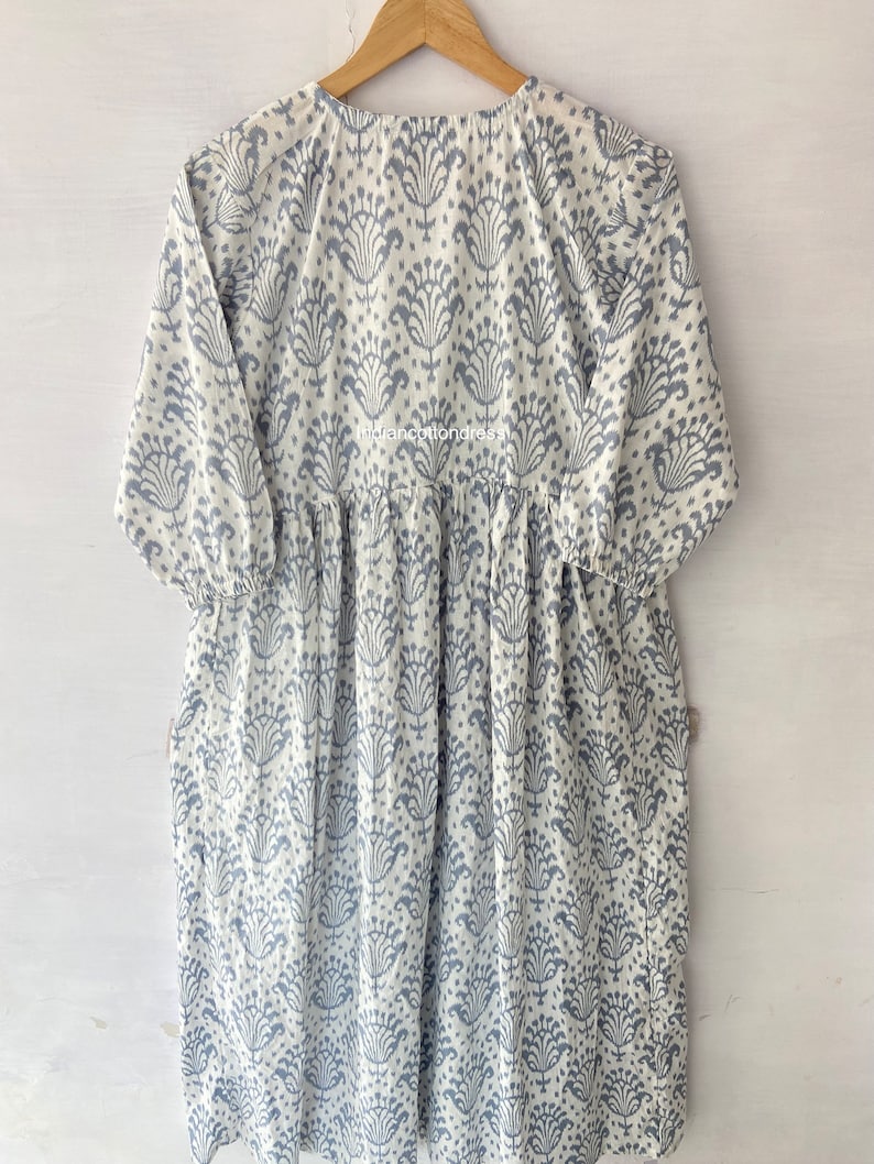 May include: A white cotton dress with a blue floral print. The dress has a round neckline and 3/4 sleeves. The dress is gathered at the waist and has a flowing skirt.