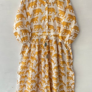 May include: A white cotton dress with a yellow tiger print. The dress has a button-up front, 3/4 sleeves, and a drawstring waist.