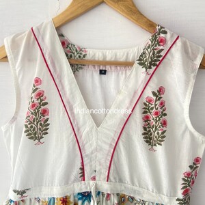 May include: White sleeveless dress with a V-neckline and floral print. The dress has red trim along the neckline and a size tag that says "M".