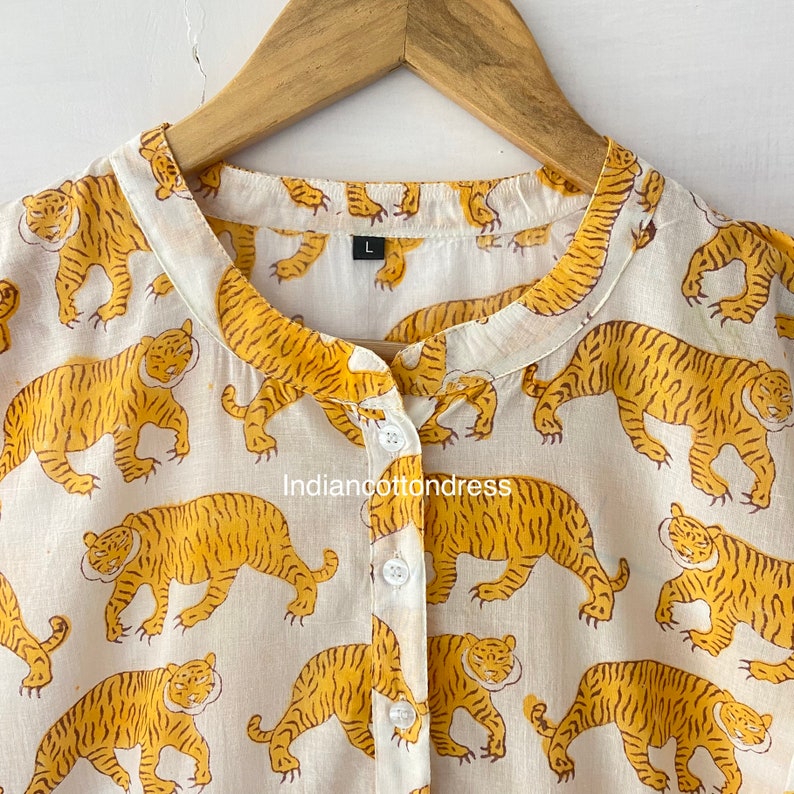 May include: White cotton shirt with a mandarin collar and button closure. The shirt features a repeating pattern of yellow tigers on a white background. The shirt is labeled size "L".