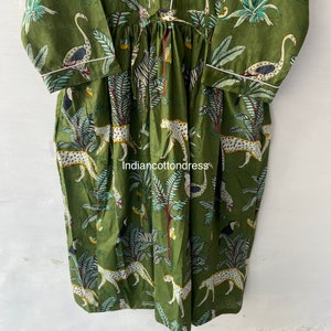 May include: A green cotton dress with a white trim. The dress features a jungle print with leopards, zebras, toucans, and flamingos.