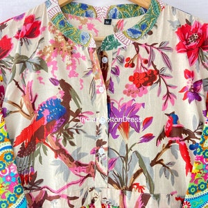 May include: A beige cotton dress with a floral print featuring birds and flowers. The dress has a button-up front and a ruffled hem. The sleeves are long and have a colorful paisley print. The dress has a size tag that says "M".