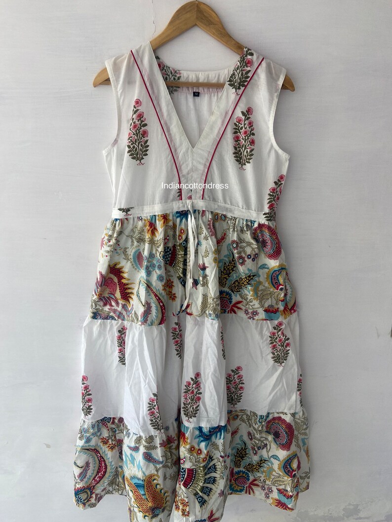 May include: White sleeveless dress with a V-neckline and a tiered skirt. The dress has a floral print in shades of pink, blue, and yellow. The neckline is trimmed with a red ribbon. The dress is made of cotton and is perfect for summer.