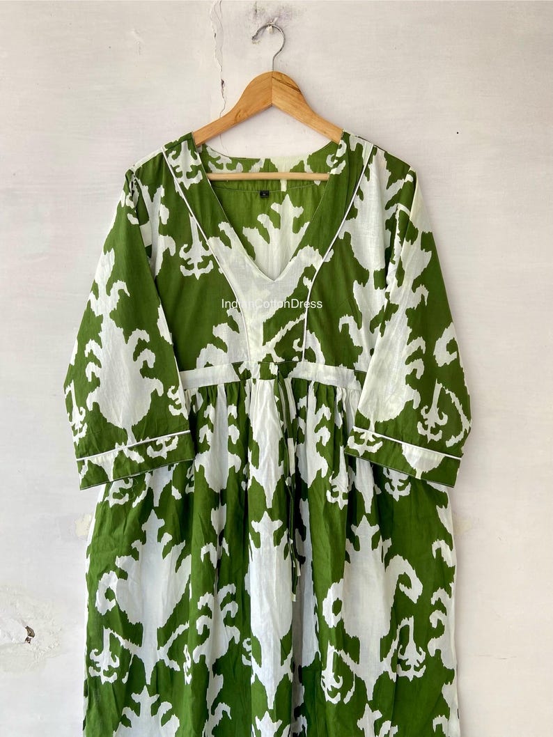 May include: A green and white cotton dress with a V-neck and 3/4 sleeves. The dress has a floral pattern and a drawstring waist. The text "IndianCottonDress" is visible on the dress.