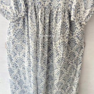 May include: A white cotton dress with a blue floral pattern. The dress has a V-neckline and 3/4 sleeves. The dress is gathered at the waist and has a flowy skirt.