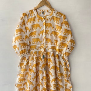 May include: A white cotton dress with a yellow tiger print. The dress has a button-up front and a drawstring waist.
