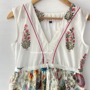 May include: White sleeveless dress with a V-neckline and a floral print. The dress has a tie at the waist and a red trim around the neckline. The dress is made of cotton and is available in size M.