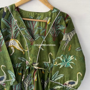 May include: A green cotton dress with a white trim and a jungle print featuring zebras, leopards, flamingos, and palm trees. The dress has a V-neck and a tie at the waist.