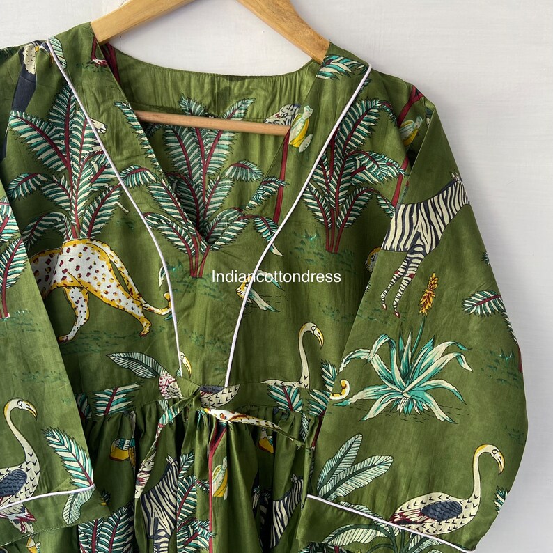 May include: A green cotton dress with a white trim and a jungle print featuring zebras, leopards, flamingos, and palm trees. The dress has a V-neck and a tie at the waist.