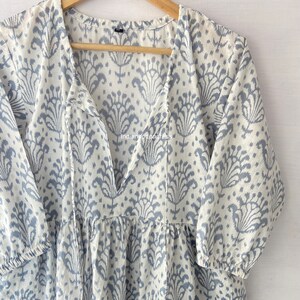 May include: A white cotton dress with a blue floral print and a V-neckline. The dress has a tie at the neckline and 3/4 sleeves.