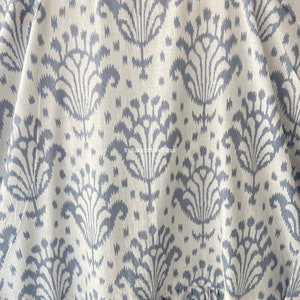 May include: Close-up of a white fabric with a blue floral pattern. The fabric has a subtle texture and a slightly distressed look. The pattern is a repeating design of stylized flowers with a central stem and multiple petals.