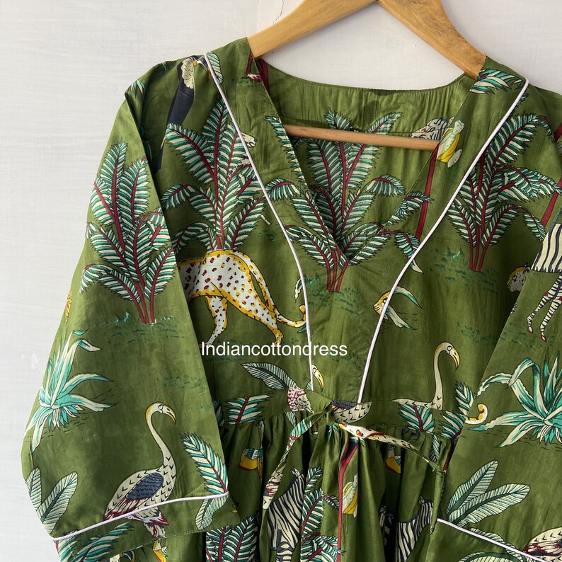 May include: A green cotton dress with a white trim. The dress features a jungle print with zebras, leopards, toucans, and palm trees. The dress has a V-neckline and a tie at the waist.